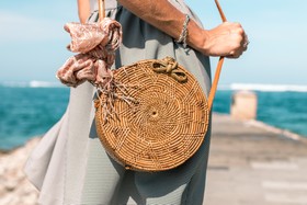 妇女身穿灰色裙子和圆形褐藤交叉袋在木箱码头附近的水体